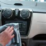 Car owner inspects a pet odor stain in a hatchback cargo area beside visible pet hair.